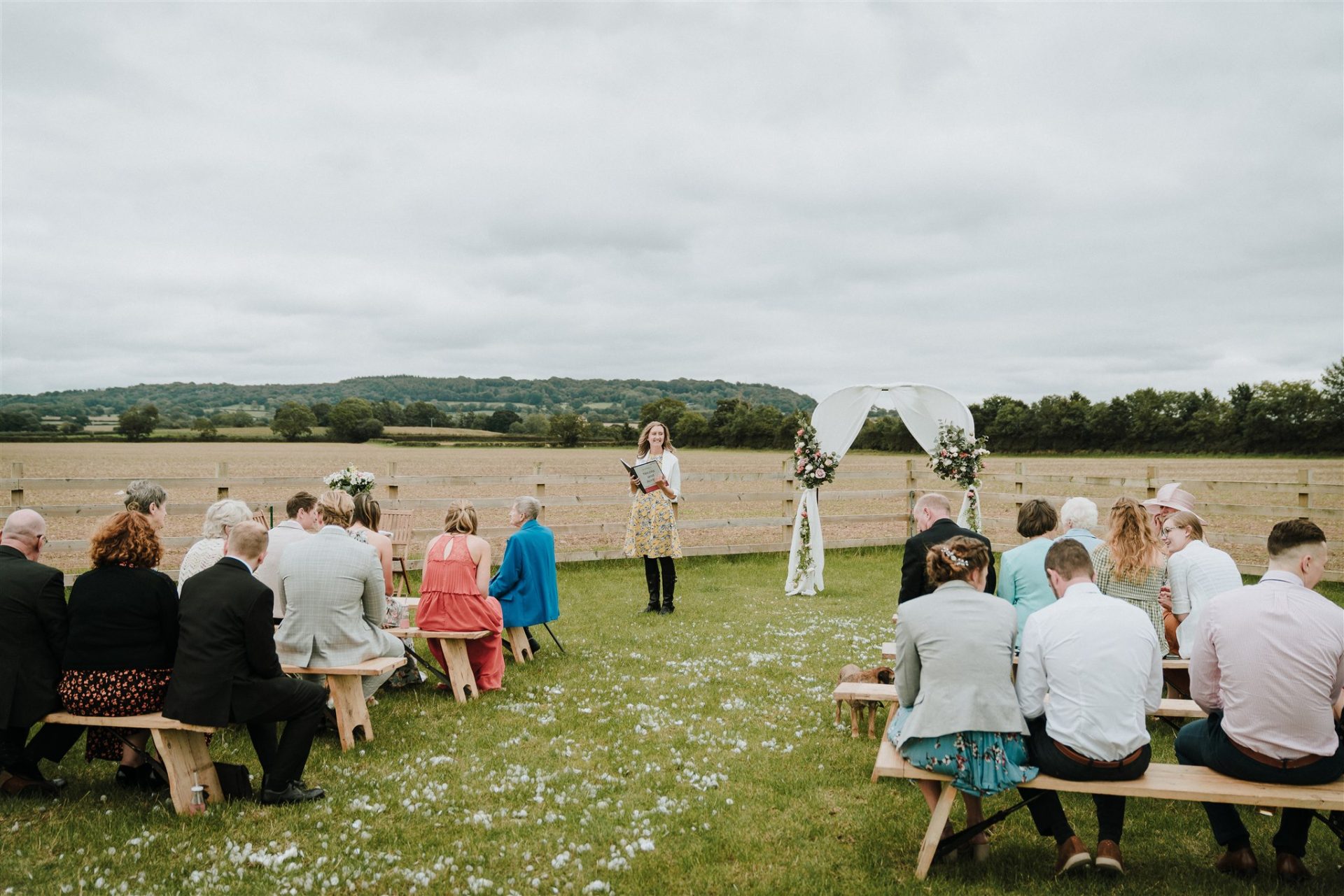 Guests on benches for Amber and Nicola's field wedding ceremony in Payhembury