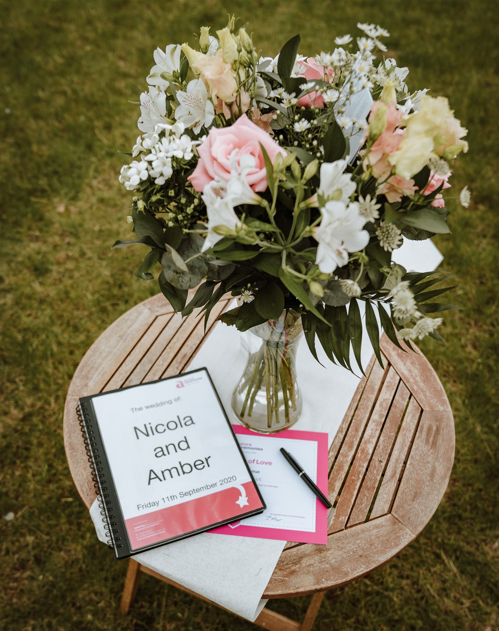 Wedding flowers and the ceremony sign on a table at Amber and Nicola's wedding