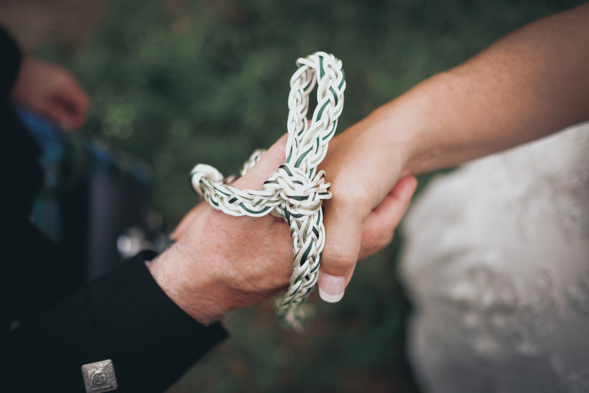 Close-up of a couple’s hands tied with cord during a handfasting ceremony
