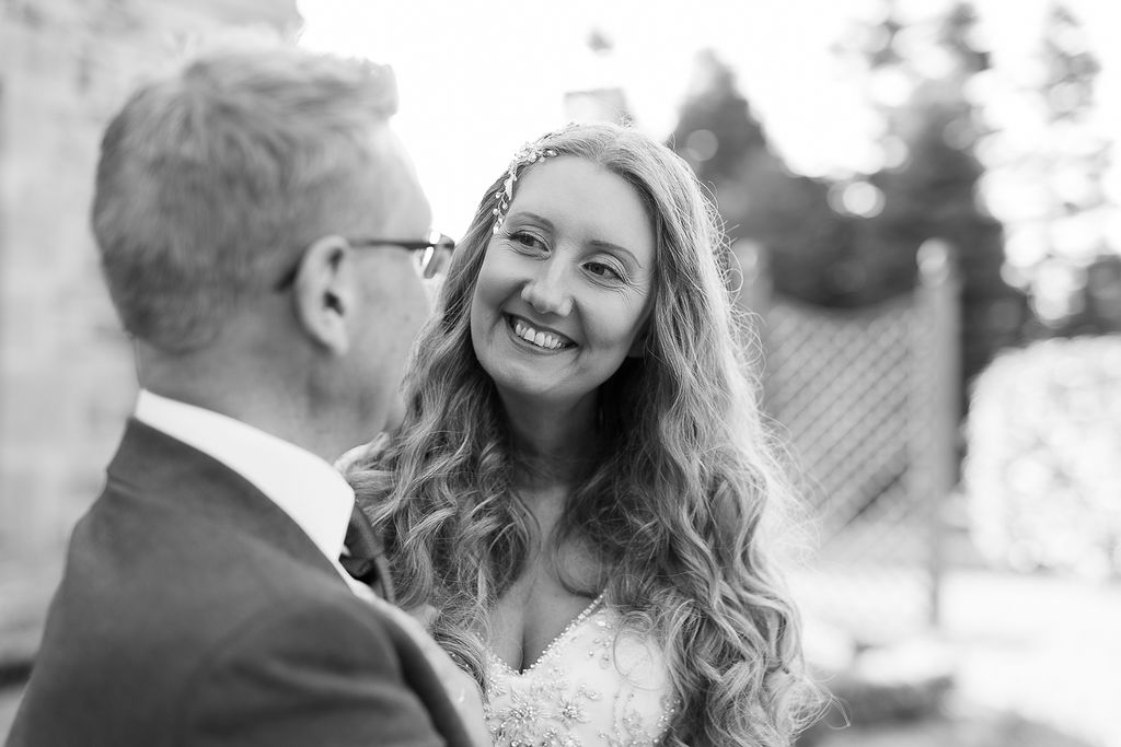 Julie Fox smiling at her husband on their wedding day, in black and white
