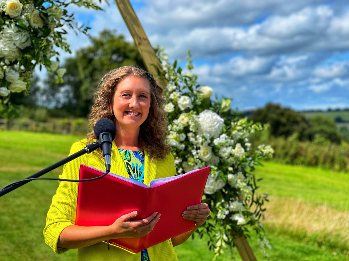 Celebrant Julie Fox leading an outdoor wedding ceremony, holding her red ceremony folder
