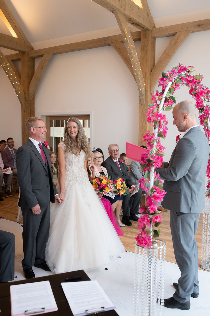 Julie Fox's wedding ceremony beneath a floral arch in the oak barn at Glebe Barn