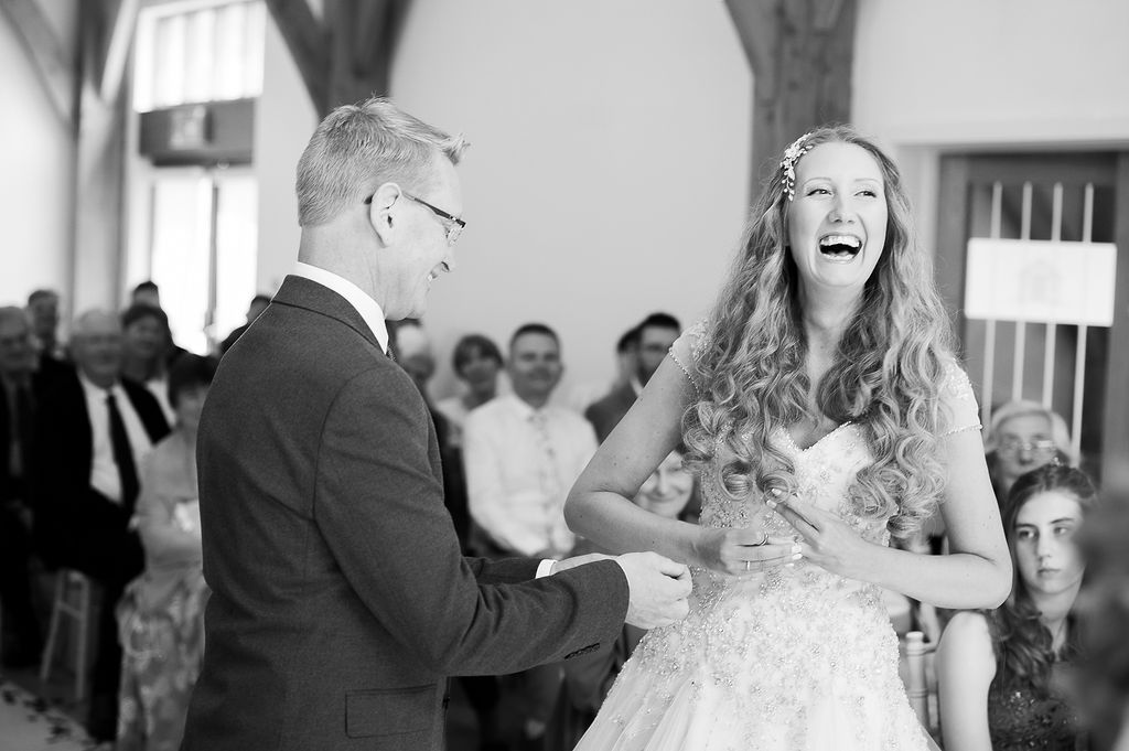 Julie Fox laughing during her wedding vows at Glebe Barn, in black and white