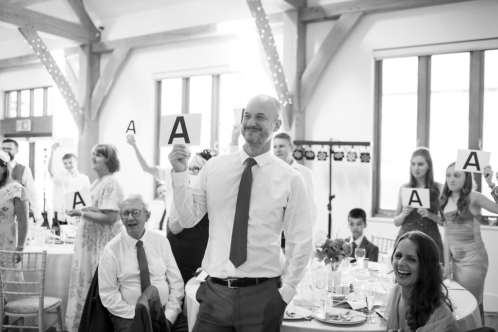 Guests holding up answer cards for the Mr and Mrs game at Julie Fox's wedding, in black and white